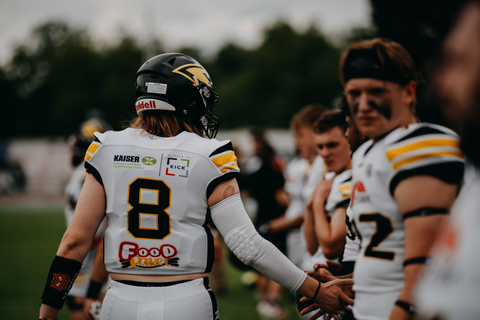 Footballspieler der Ravens klatschen sich auf dem Spielfeld ab. Auf dem Trikot eines Spielers ist das Foodpaket-Logo als Sponsor zu sehen.