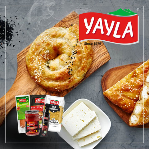 Vorschaubild zur Marke Yayla mit dampfendem Blätterteiggebäck mit Käsefüllung auf Holzbrett, daneben Produktfotos von Bulgur, Granatapfelsirup und veganer Sucuk – oben rechts das Yayla-Logo.